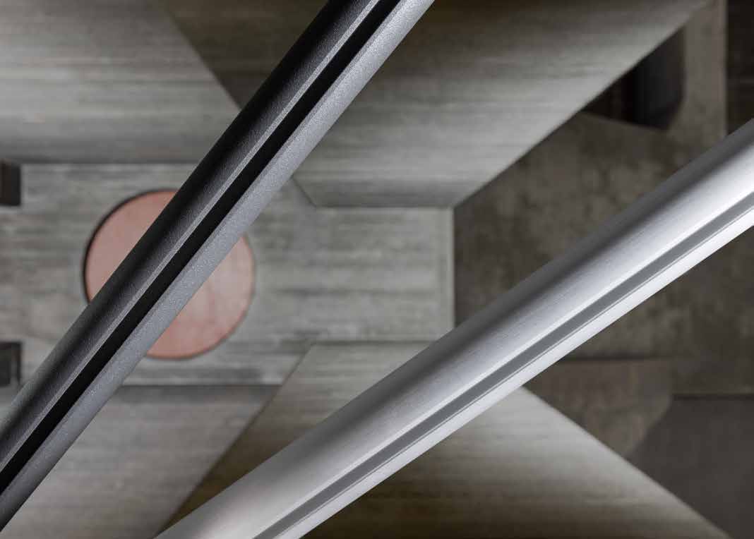 Onderzijde van een donker SLIDE-profiel met zichtbare geleidingssleuf, boven een zilverkleurige rail Onderzijde van een donker SLIDE-profiel met zichtbare geleidingssleuf, boven een zilverkleurige rail.