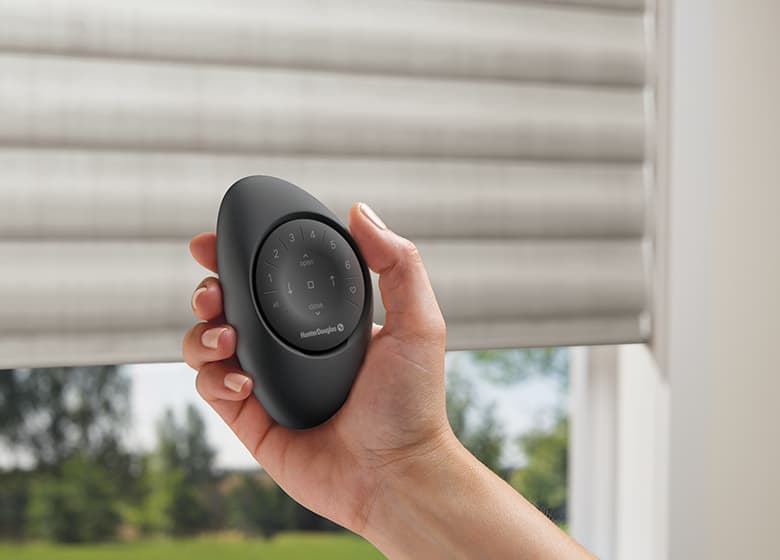 Hand met zwarte PowerView Remote in een zwarte Pebble-huls, met raamdecoratie op de achtergrond Hand met zwarte PowerView Remote in een zwarte Pebble-huls, met raamdecoratie op de achtergrond.