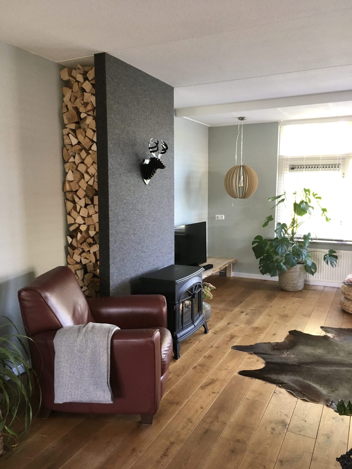 Hollandfelt – grijze wolvilten wand in een woonkamer Woonkamer met grijze wolvilten wand, fauteuil en kachel